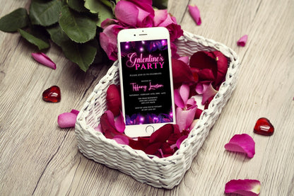 Cell phone in a basket of rose petals showcasing the Purple Pink Neon Palm Leaves Galentines Party Evite template for customization via Canva.