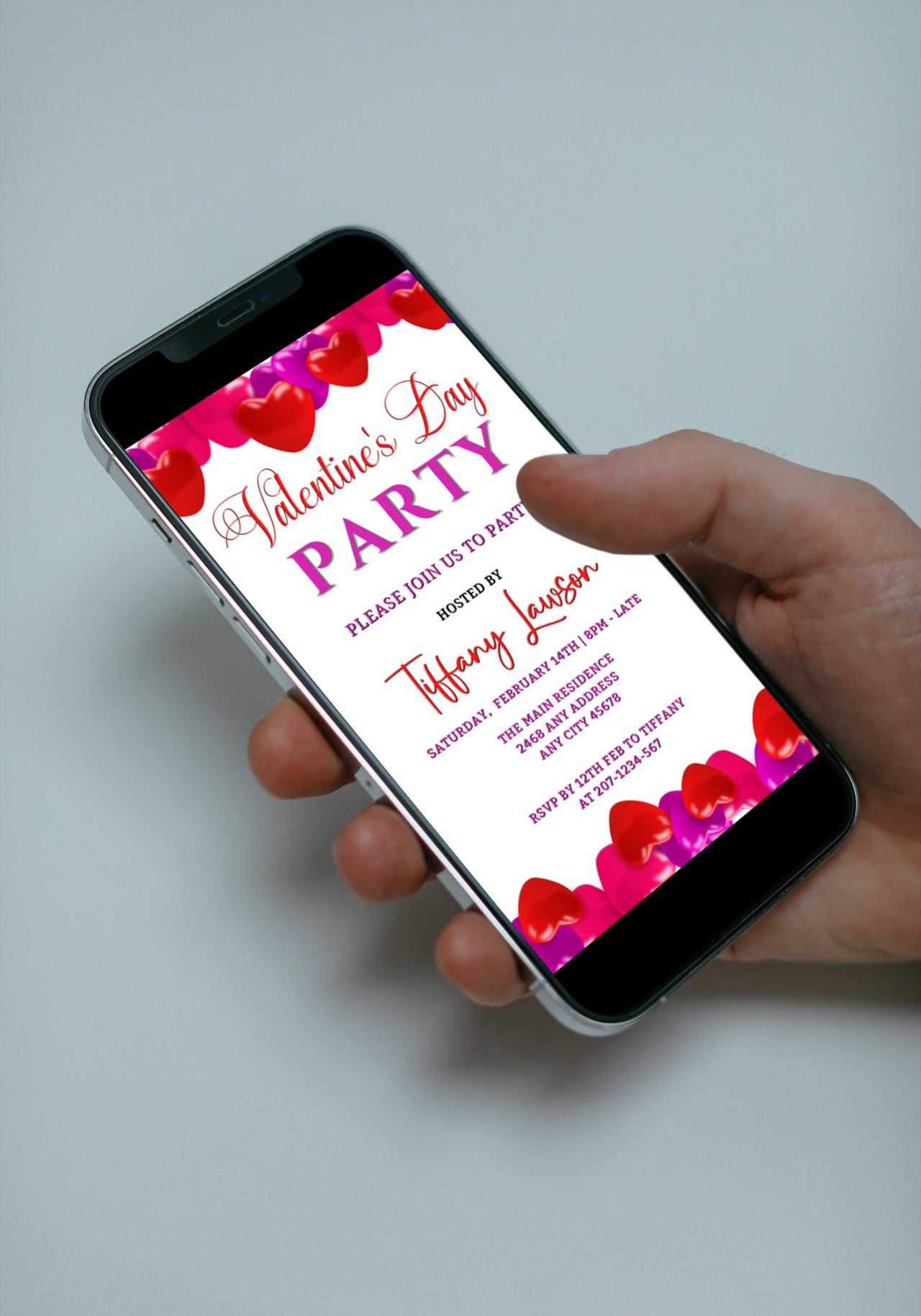 Hand holding a smartphone displaying a customizable Pink Red Hearts Valentine's Party Evite, editable via Canva for digital invitations.