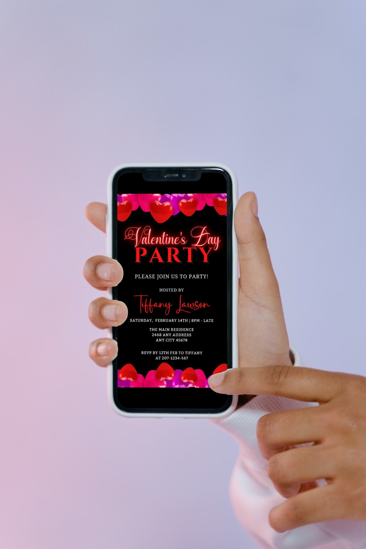 Hand holding a smartphone displaying a customizable digital invitation template with black, pink, and red hearts for Valentine's Day parties, available for editing in Canva.