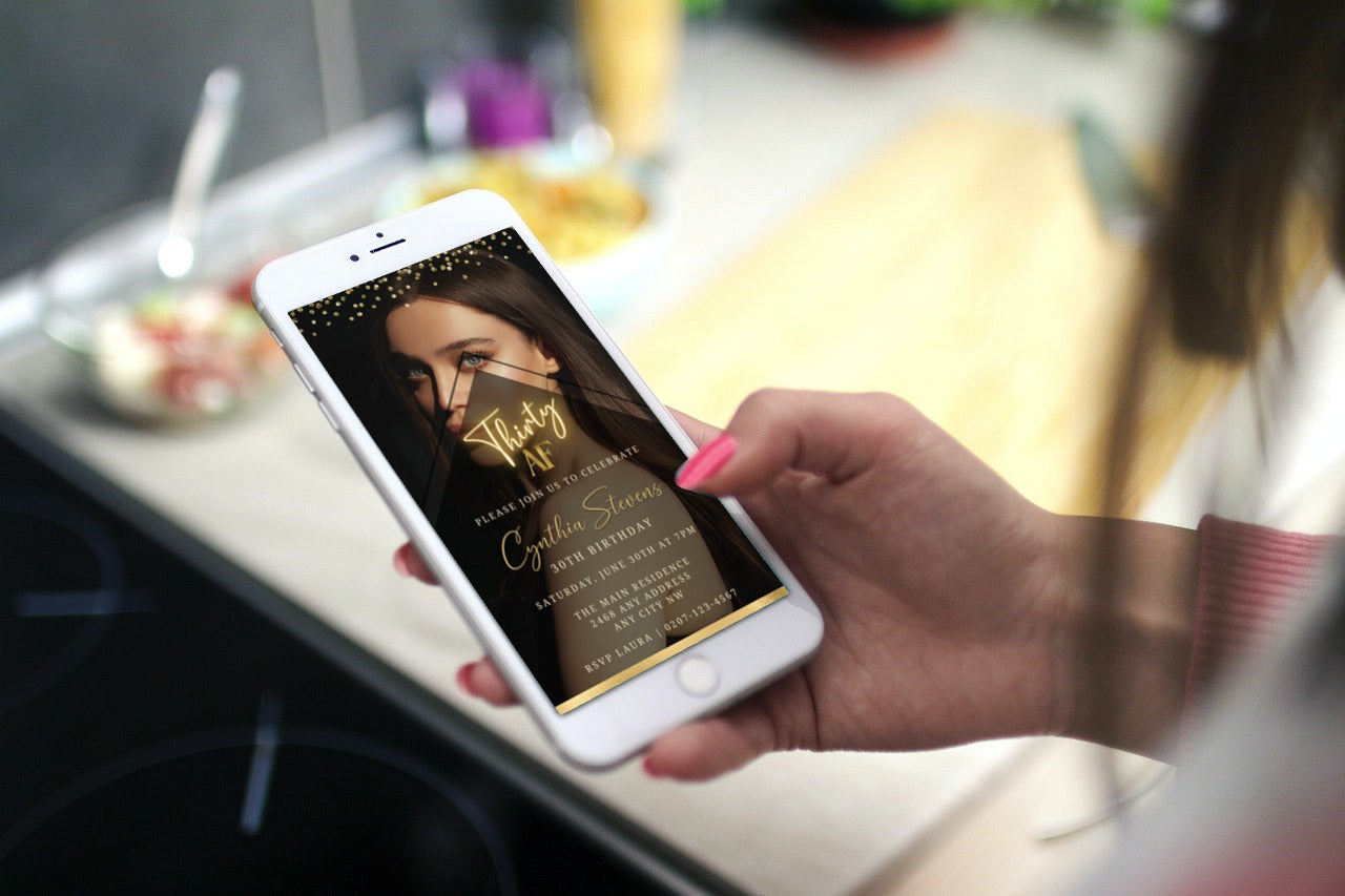 A hand holding a smartphone displaying the customizable Digital Photo Background Gold | 30AF Birthday Evite template from URCordiallyInvited.