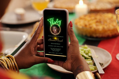 Person holding a smartphone displaying a customizable digital Oval Gold Photo Frame Neon, 30th Birthday Evite.