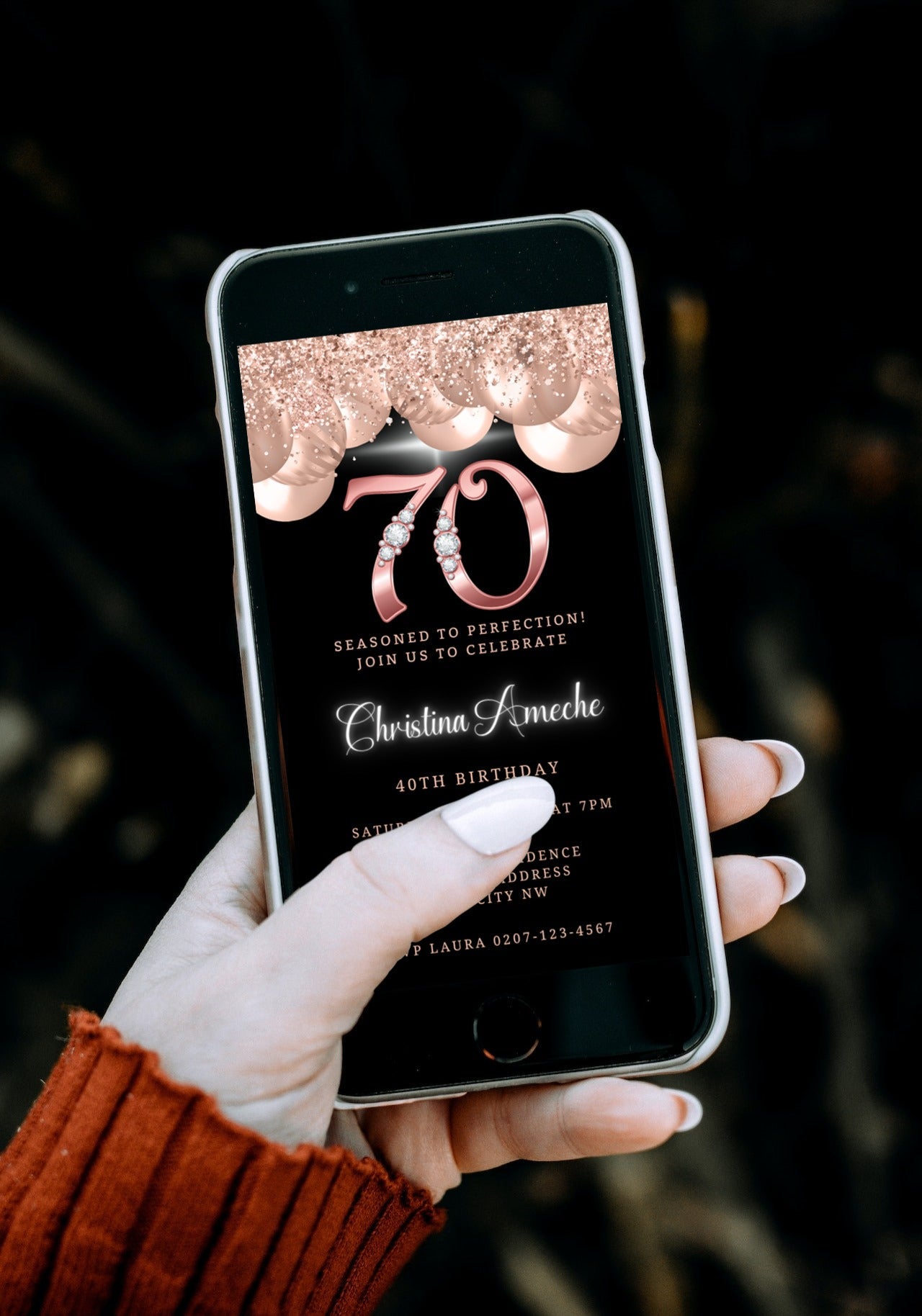 A hand holding a smartphone displaying the customisable Rose Gold Balloons Diamond Studs | 70th Birthday Evite template.