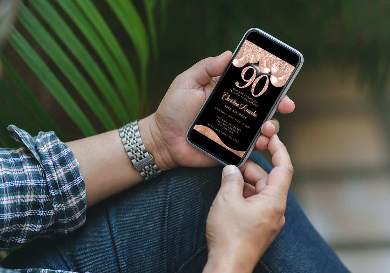 Person holding a smartphone displaying a customizable Rose Gold Balloons Glitter 90th Birthday Evite template from URCordiallyInvited.