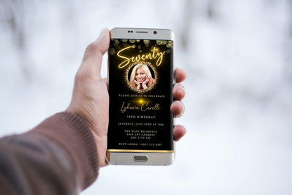 Hand holding a smartphone displaying a customizable Digital Gold Neon W/Oval Photo Frame for a 70th Birthday Evite.