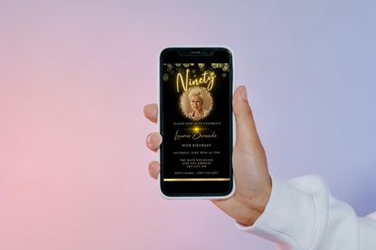 Hand holding a smartphone displaying a customizable digital Gold Neon W/Oval Photo Frame 90th Birthday Evite template with a woman's photo.