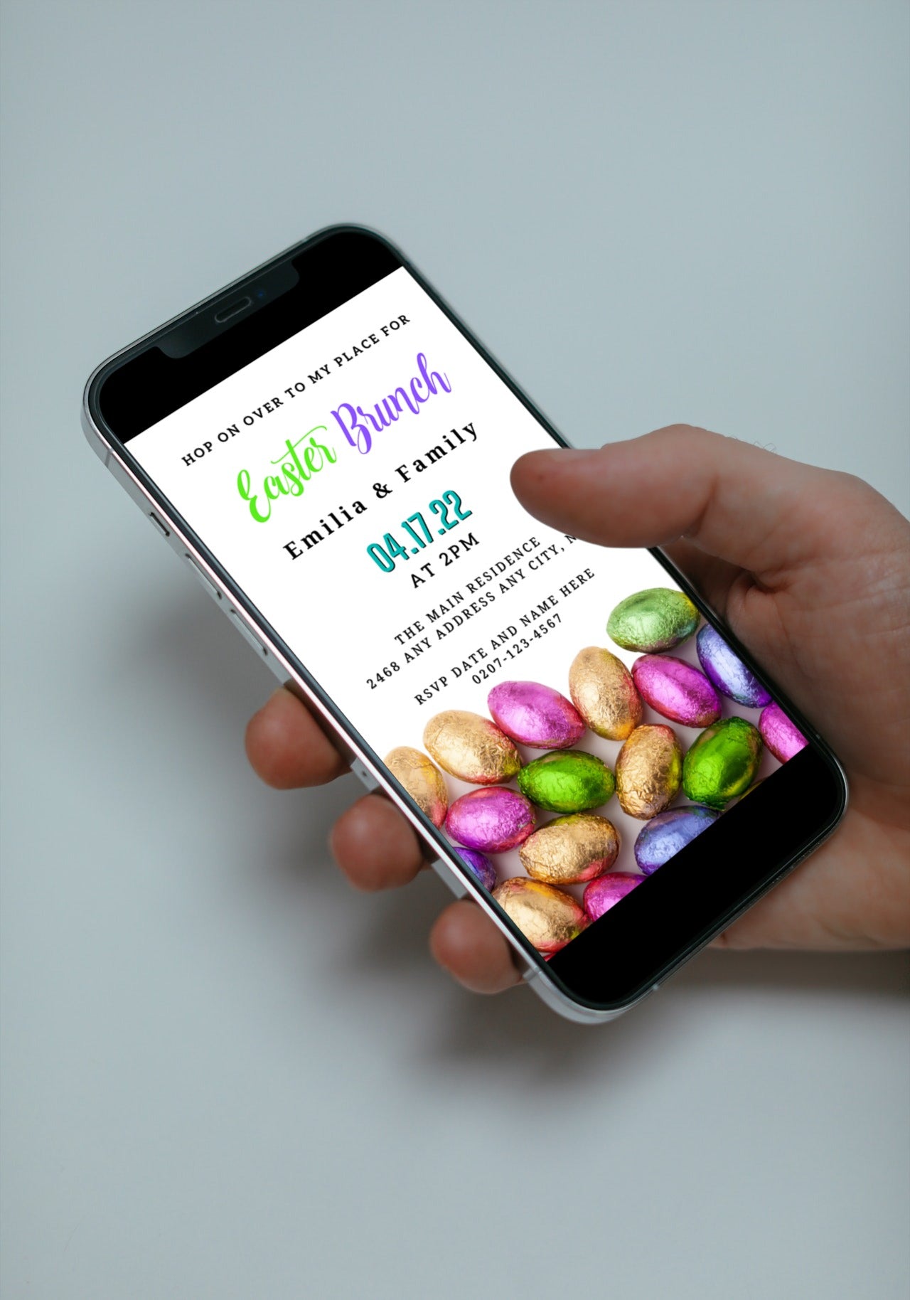 Hand holding a smartphone displaying a Colourful Assorted Chocolate Easter Eggs | Easter Brunch Evite template.