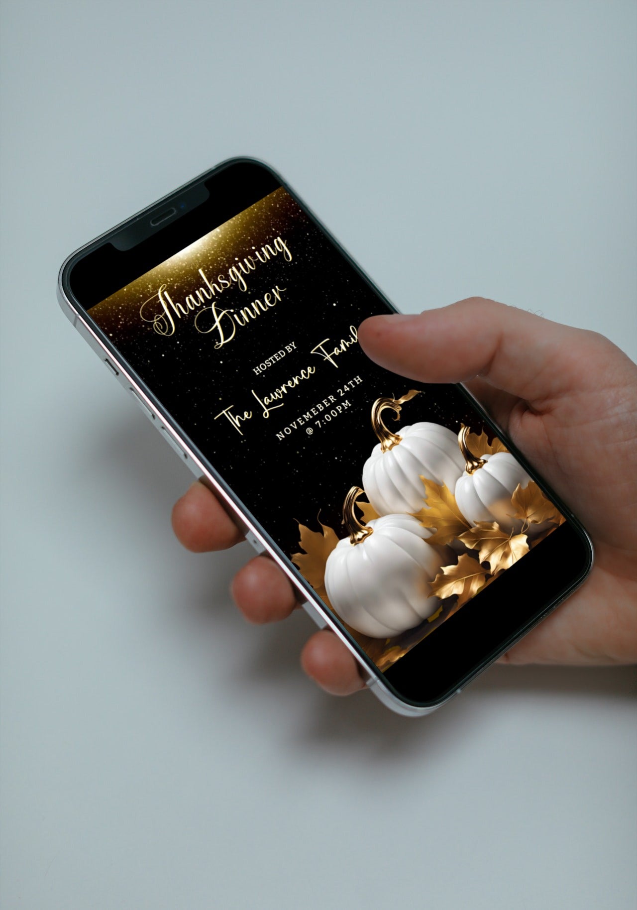 Hand holding a cell phone displaying the Gold Glitter Neon White Pumpkins Thanksgiving Dinner Video Invite template for customization.