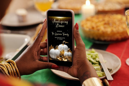 Person holding a phone displaying the Gold Glitter Neon White Pumpkins Thanksgiving Dinner Video Invite template.