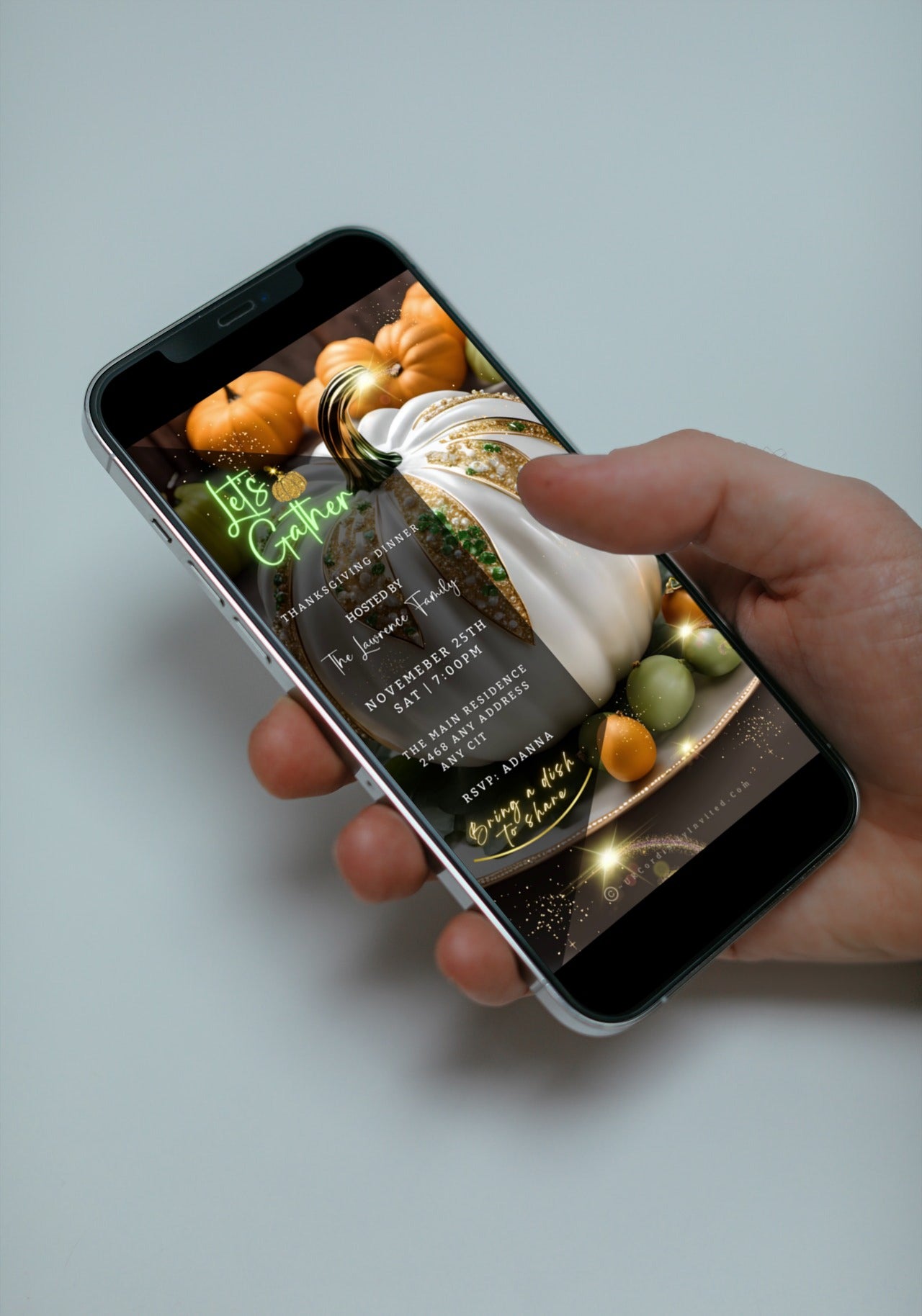 Hand holding a smartphone displaying the White Fruitful Platter Glitter Pumpkin Thanksgiving Dinner Video Invite template for customization on Canva.