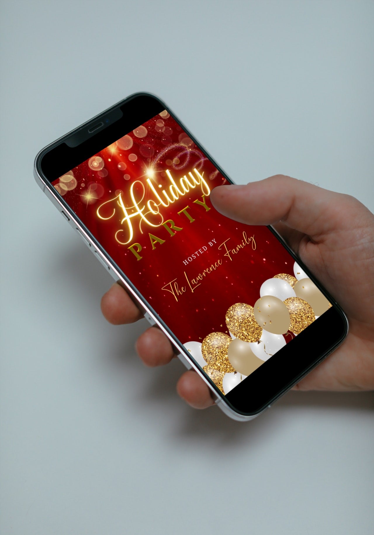 Hand holding a smartphone displaying a customizable Red Gold Glitter Balloons Sparkle Christmas Video Invitation template from URCordiallyInvited. The phone shows festive balloons.