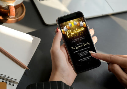 Person holding a phone displaying a customizable digital Christmas party video invite with snowy gold and white ornaments, designed for editing and sharing via mobile devices.