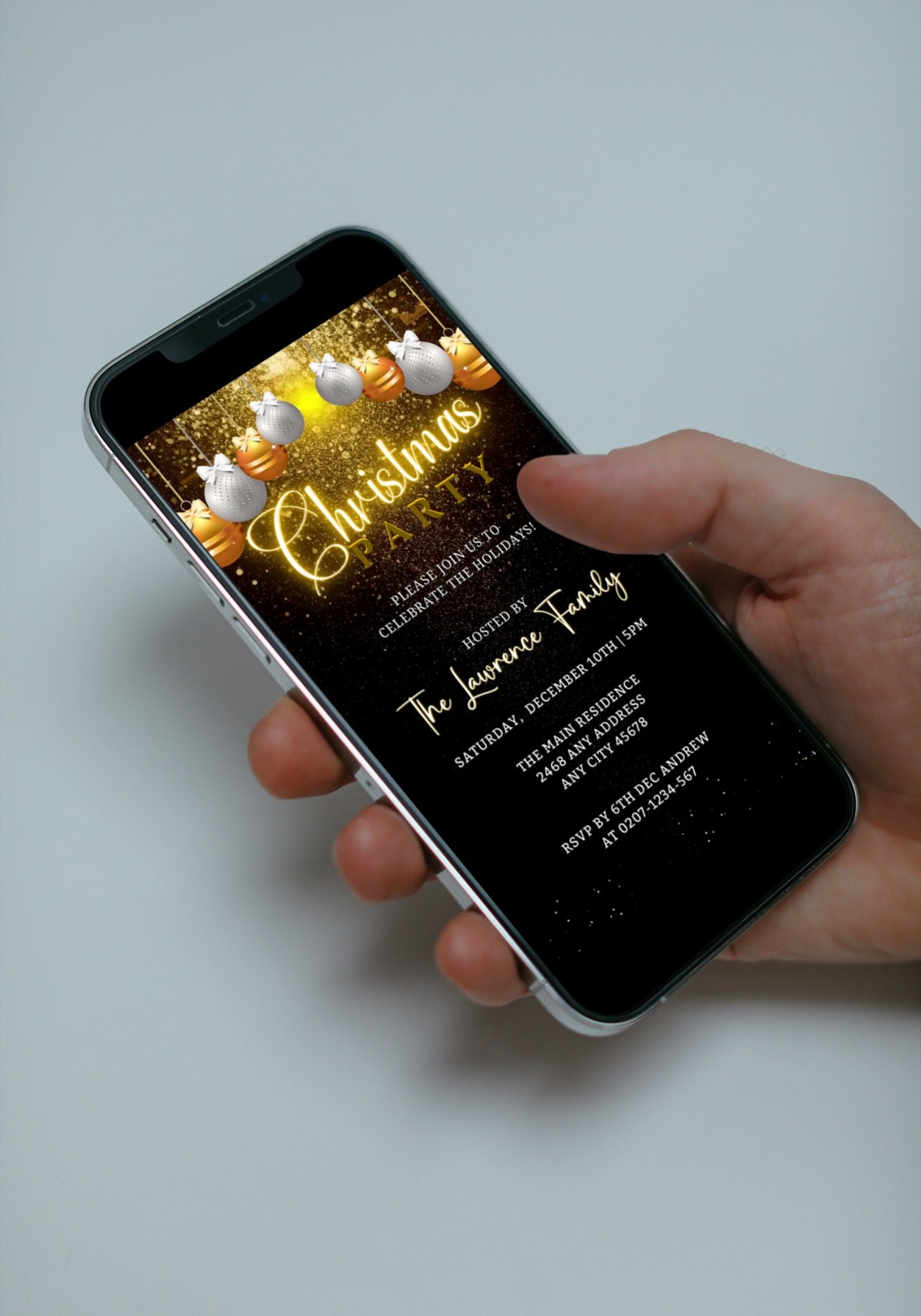 Hand holding a smartphone displaying a Snowy Gold White Ornaments Glitter Christmas Party Video Invite template for customization.