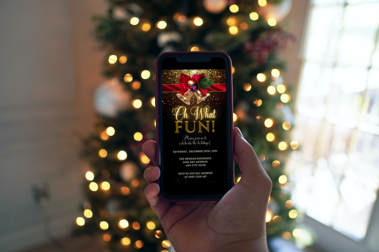 A hand holding a phone displaying the Golden Snow Ribbon Glitter Christmas Party Video Invite, with a Christmas tree in the background.