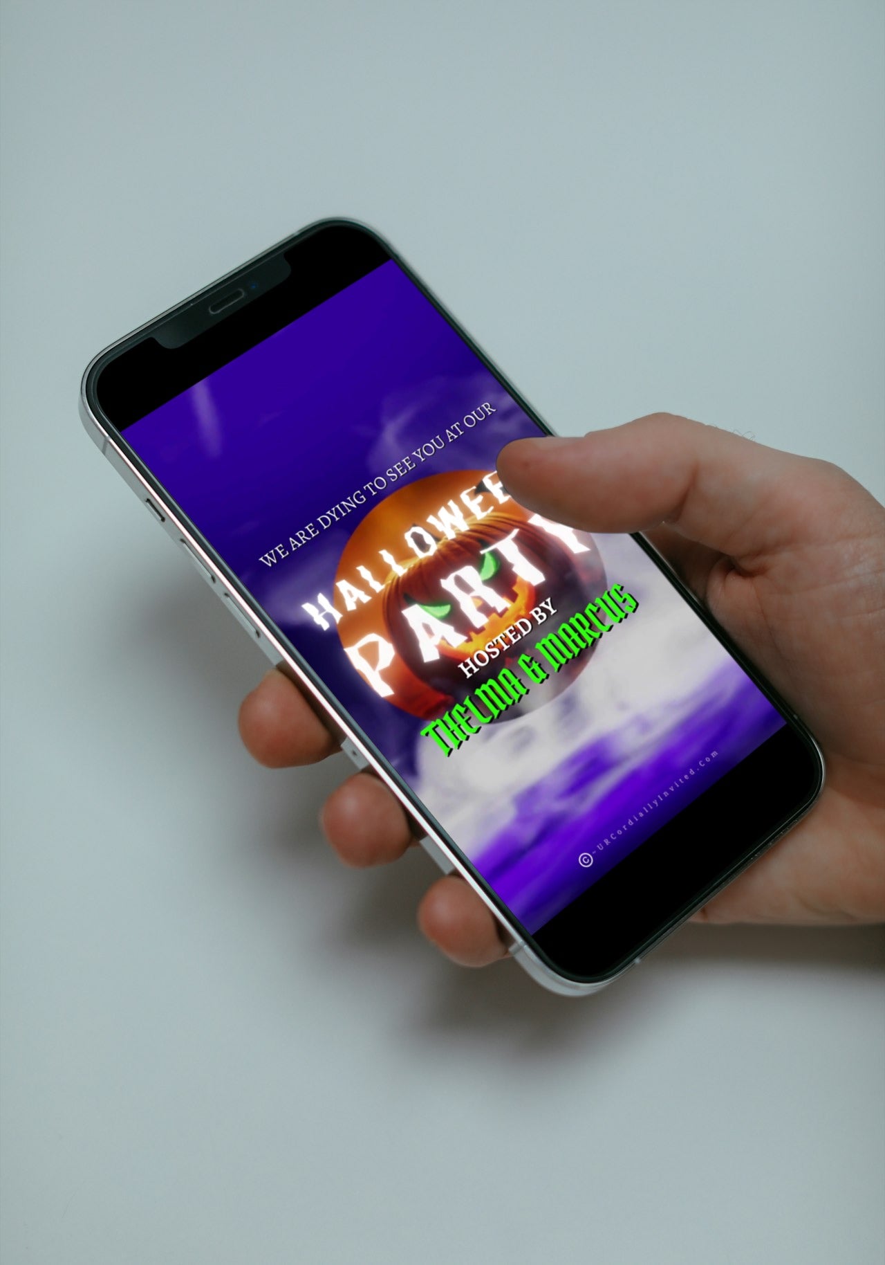 Hand holding a smartphone displaying the Misty Purple Smoke Pumpkin Halloween Party Video Invite, featuring an animated pumpkin with swirling purple smoke.