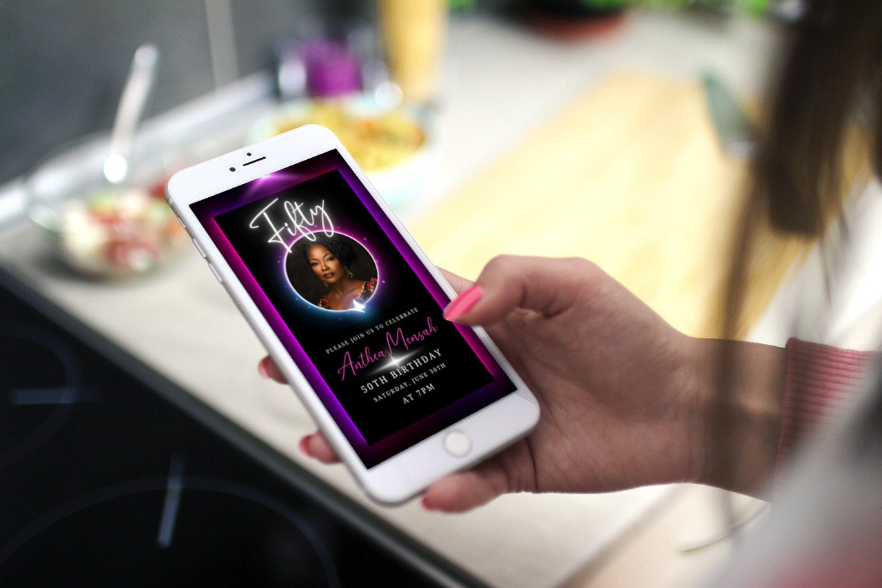 Hand holding a phone displaying the 50th Birthday Video Invitation featuring a pink and purple oval photo frame, designed for customizable digital invites via Canva.