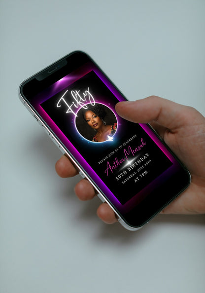 A hand holding a smartphone displays a 50th Birthday Video Invitation featuring a woman's photo inside a neon pink and purple oval frame.