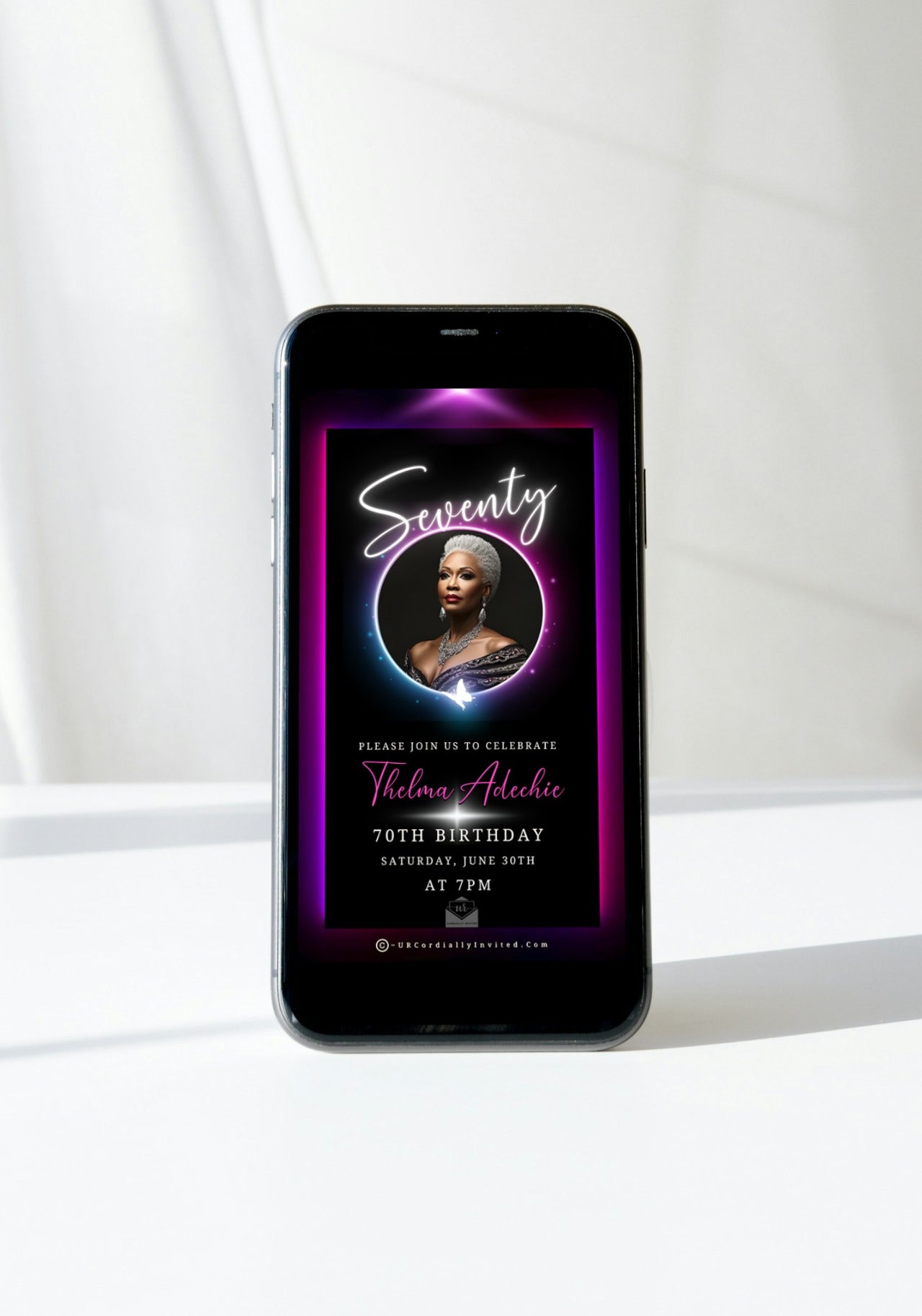 70th Birthday Video Invitation with a woman’s photo in a glowing pink and purple oval frame on a mobile phone screen.