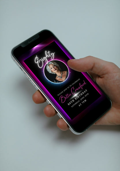 Hand holding a mobile phone displaying the 80th Birthday Video Invitation with a pink and purple oval photo frame, highlighting the celebrant’s image.